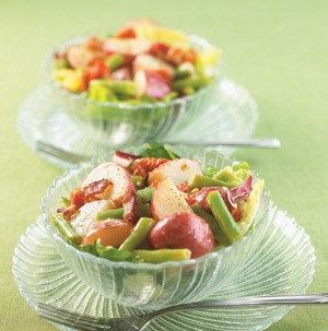 Halved baby red potatoes with green beans and bacon in crystal serving dishes with forks