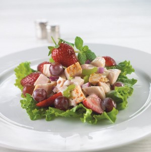 Chicken cubes with strawberries, grapes, and mint on a lettuce leaf