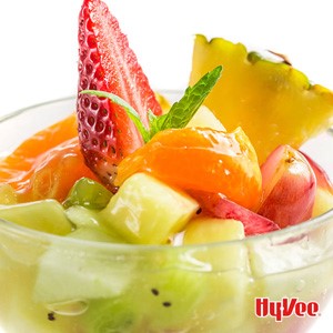 Clear bowl of fruit salad with pineapple, kiwi, grapes, strawberries and bananas