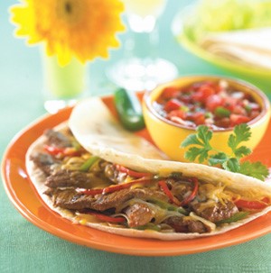 Shredded beef and pepper fajitas on an orange plate with pico de gallo in the background