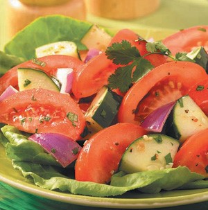 Tomato wedges with red onions and cucumbers on top of a lettuce leaf