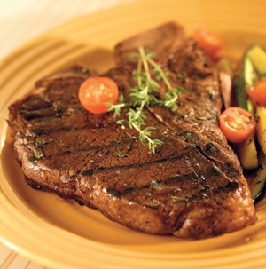 T-bone steak grilled in balsamic garlic with grape tomatoes on a yellow plate