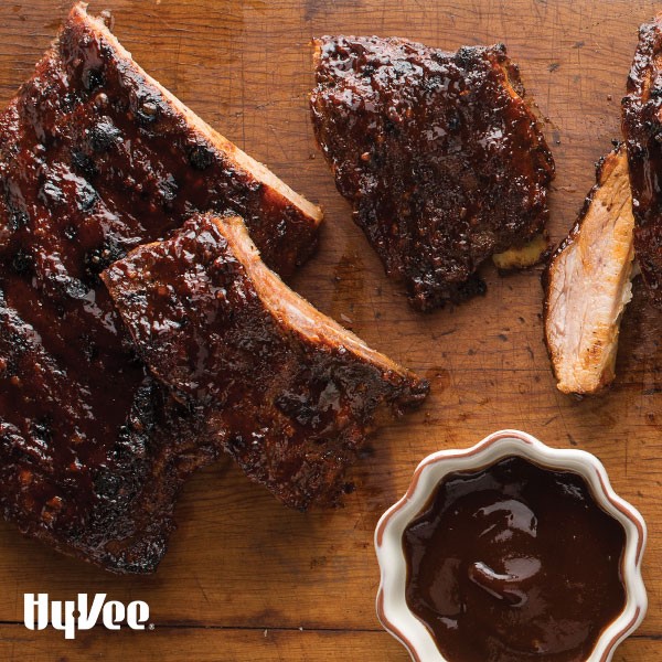 Wood cutting board with sliced rack of pork ribs and barbecue sauce on the side