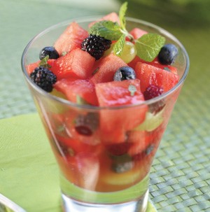 Glass filled with cubed watermelon, fresh blackberries, raspberries, and green grapes with fresh mint leaf garnish