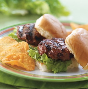 Bun topped with lettuce and grilled burger with a side of potato chips