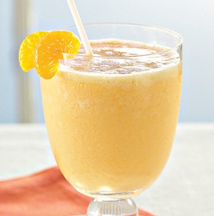 Glass filled with an orange-colored smoothie, garnished with orange slices and a straw