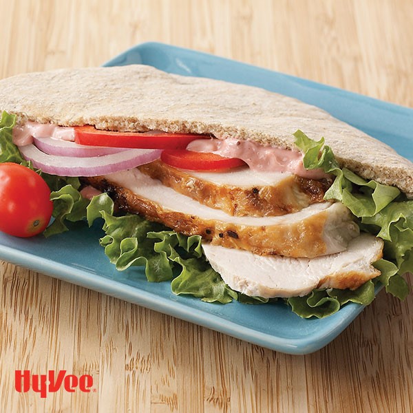 Pita pocket filled with sliced turkey, lettuce, tomatoes, and red onion slices on a blue plate