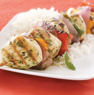 Chicken and vegetable kabobs in pesto glaze over a bed of white rice on a white plate