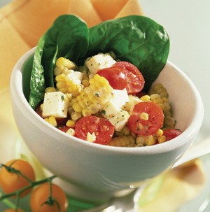 White bowl filled with corn, mozzarella cubes, halved tomatoes, and spinach leaves