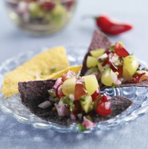 Blue and yellow tortilla chips topped with diced red onions and halved red and green grapes