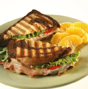 Marbled rye bread with cheese, tomato, turkey, lettuce, and a side of orange segments on a grey plate