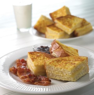 Havarti stuffed french toast on white plate with sliced crisped bacon on the side