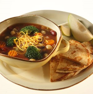 Soup filled with carrot coins, broccoli florets, and shredded cheese with a side of sliced pears and pita triangles