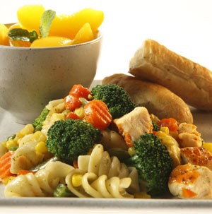 Spiral pasta filled with corn, carrot coins, broccoli and chicken with a side of sliced fruit and bread