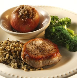 Apple-glazed pork chops served with rice, broccoli and a stuffed apple on a white plate