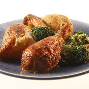 Rotisserie chicken drumsticks on a dark blue plate with broccoli