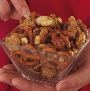 Hands holding a bowl of nuts, chex and pretzels