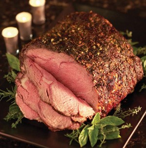 Whole herb-crusted sliced rib eye roast surrounded by fresh herbs