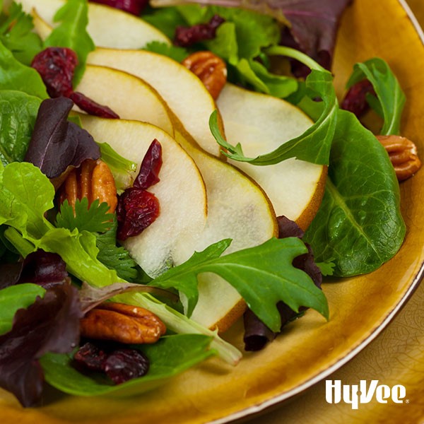 Mixed green salad topped with halved pecans, dried cranberries, and sliced skin-on pears