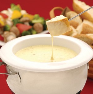 White crock pot filled with white cheese with dunked bread cube