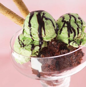 Chocolate brownie topped with scoops of mint ice cream and chocolate sauce in a clear dish