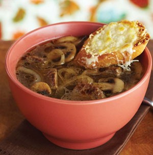 Peach-colored bowl filled with french onion soup and topped with a cheesy-toasted baguette slice