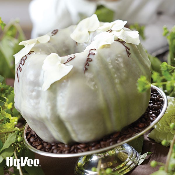 White chocolate bundt cake decorated with flour petals and chocolate vines surrounded by green and white flowers