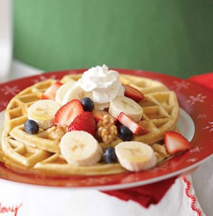 Two waffles topped with strawberries, sliced bananas and blueberries with whipped cream on top