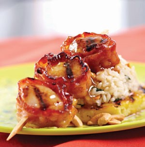 Skewered grilled scallops wrapped in bacon with rum glaze on a plate with rice 