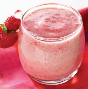 Glass filled with pink raspberry banana smoothie with whole strawberry and raspberry on rim