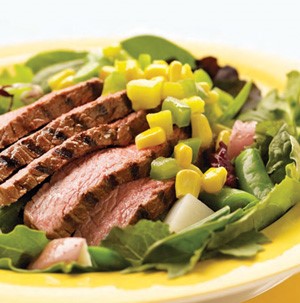 Grilled and sliced steak with corn kernels, green peppers and pea pods on a bed of lettuce