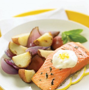 White plate filled with potato wedges, red onion wedges, grilled salmon with a dollop of lemon-garlic sauce