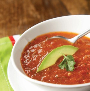 Red gazpacho topped with sliced avocado and fresh herbs for garnish