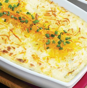 White casserole dish filled with browned twice baked potatoes topped with melted cheese and sliced green onions