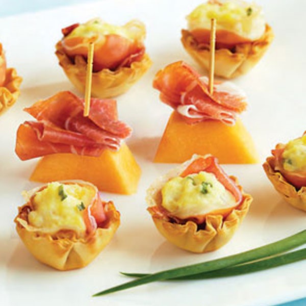 Prosciutto-cheese bites next to cantaloupe and prosciutto on toothpicks 