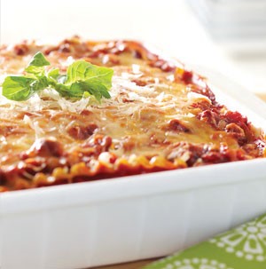 White casserole dish filled with layered lasagna and garnished with fresh herbs and melted cheese