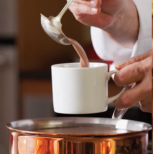 Pouring hot cocoa into white mug over copper saucepan