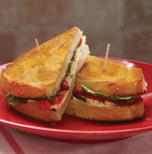 Toasted sandwiches filled with red pepper, sliced meat. and lettuce leaves on a red plate