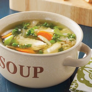 Chicken soup with peas, chopped celery and carrots, and grains in white serving dish