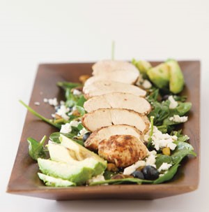 Plate of spinach topped with chicken, blueberries, avocado, feta and pistachios