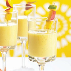 Wine glasses filled with mango smoothies and garnished with cubed mango pieces on a wooden skewer