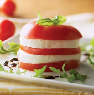 Stacked sliced tomatoes and fresh mozzarella garnished with fresh basil, arugula, and balsamic vinegar