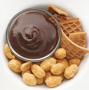 Melted chocolate in a bowl with whole peanuts and waffle cone pieces
