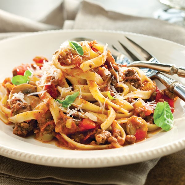 Fettuccini noodles tossed in red sauce with ground meat, basil leaves, and diced tomatoes