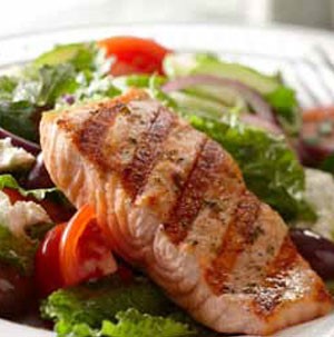 Salad filled with mixed greens, chopped tomatoes, crumbled cheese, sliced red onion, and grilled salmon fillet