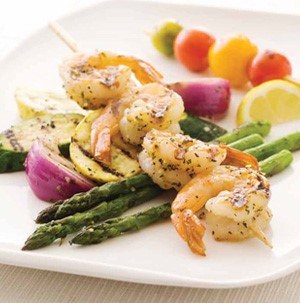 White plate topped with asparagus spears, grilled red onions and zucchini, tail-on shrimp on a skewer, and assorted cherry tomatoes on a skewer