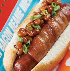 Bacon-wrapped sausage on a bun, topped with baked beans and green onions