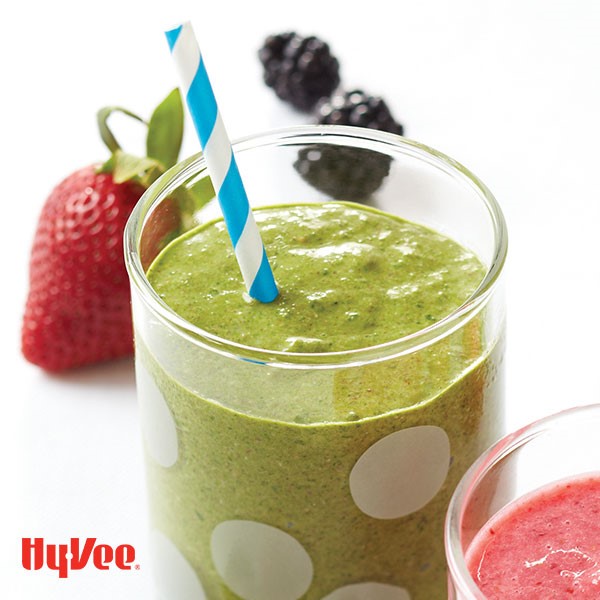 Green smoothie in a polka dot glass with a blue and white stripped straw and mixed berries on the side