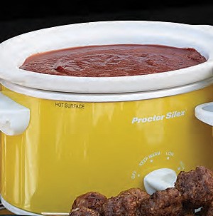 White and yellow slow cooker filled with red ham ball sauce