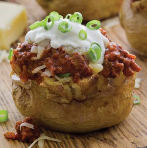 Baked potato topped with chili, sour cream, and chopped green onions on a wooden cutting board
